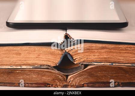 Öffnen Sie Seiten von alten schäbigen braunen und neuen Büchern, digitale Tablette. Konzept der Wahl zwischen neuen Technologien und alten Büchern. Analog oder digital. Nahaufnahme Stockfoto