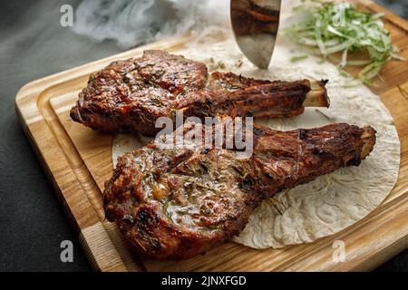 Chalagach gegrillt mit Rauch auf einem Holzbrett mit einem Messer Stockfoto