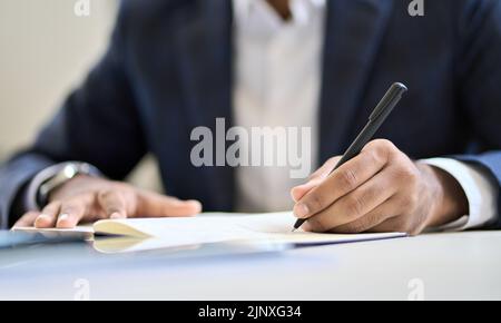 Geschäftsleiter trägt Anzug, der in einem Notizbuch oder einem juristischen Dokument verfasst ist. Stockfoto