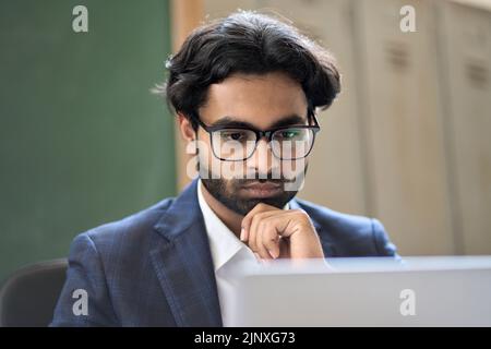 Nachdenklicher junger indischer Geschäftsmann, der Marktdaten analysiert und Computer betrachtet. Stockfoto