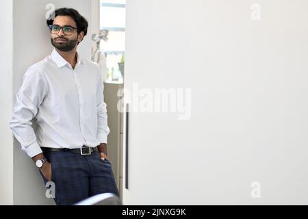 Eleganter reicher erfolgreicher junger indischer Geschäftsmann, der im Büro steht. Stockfoto