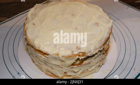 Die Hand des Mannes setzt die Creme auf den Kuchen, die Kuchendekor. Napoleonkuchen mit Creme machen. Stockfoto