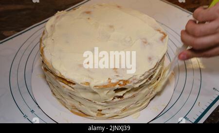 Die Hand des Mannes setzt die Creme auf den Kuchen, die Kuchendekor. Napoleonkuchen mit Creme machen. Stockfoto