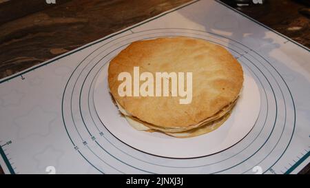 Die Hand des Mannes setzt die Creme auf den Kuchen, die Kuchendekor. Napoleonkuchen mit Creme machen. Stockfoto