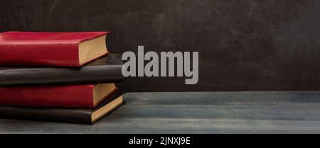 Vorlage „Zurück zur Schule“. Bücher stapeln sich auf einem blauen Holztisch im Klassenzimmer, leerer Tafelhintergrund, Platz zum Kopieren Stockfoto