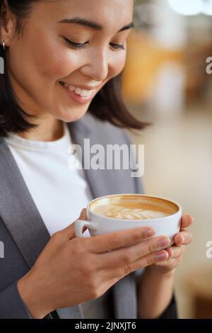 Lächelnde junge asiatische Frau hält Tasse trinken Kaffee Latte genießen Aroma. Stockfoto