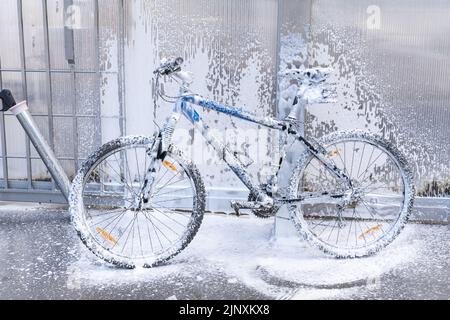 Waschen eines Fahrrads mit einem Schaumstrahl bei einer Autowäsche. Das Fahrrad ist mit Schaumstoff überzogen. Self-Service. Fahrradwartung. Stockfoto