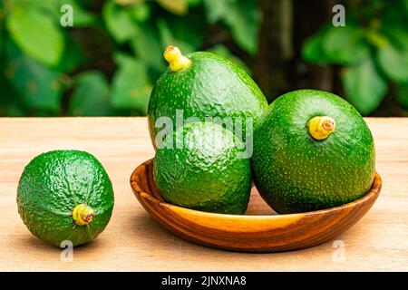 Nahaufnahme Ansicht Gruppe von frischen grünen Avocados mit Stiel in Holzplatte auf Holztisch. Stockfoto