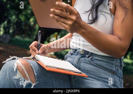 Glückliche Frau, die in einem Lehrbuch in einem Park schreibt Stockfoto