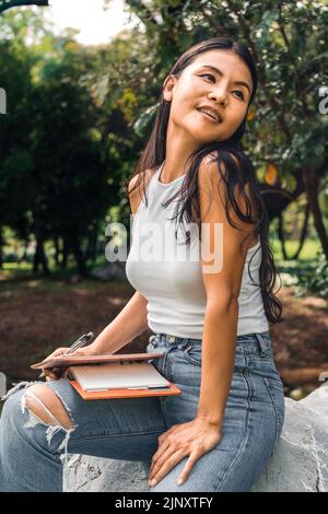 Glückliche Frau, die in einem Lehrbuch in einem Park schreibt Stockfoto