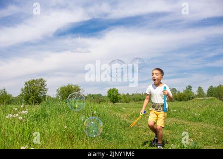 Vorschulkinder blasen an einem sonnigen Tag große Seifenblasen auf einem Feld Stockfoto