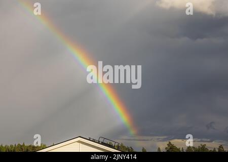 Schöner Blick auf den Regenbogen nach dem Regen über den Dächern von Mistgabeln an warmen Sommertagen. Schweden. Stockfoto