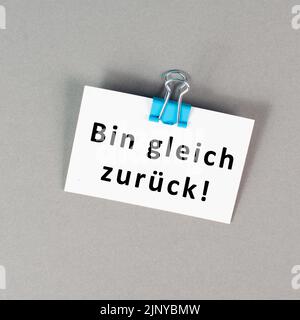 Ich komme bald wieder steht in deutscher Sprache auf einem Papier, macht eine Pause, hinterlässt eine Nachricht auf dem Schreibtisch Stockfoto