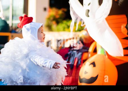 Kleinkind trägt ein Hühnchen-Halloween-Kostüm vor einem aufblasbaren Geist auf einer Halloween-Party in Fountain Hills, Arizona. Stockfoto