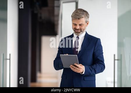 Modernes Technologiekonzept. Lächelnder, Reifer Geschäftsmann Trägt Anzug Mit Digitalem Tablet Im Innen-Bereich Stockfoto