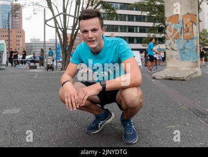 Hamburg, Deutschland. 14. August 2022. Der 16-jährige Student Denis Holub hockt am Boden, nachdem er die Ziellinie seines 1100 Kilometer langen Charity-Laufs von Freiburg nach Hamburg überquert hat. Mit seinem Lauf unterstützt der Gymnasiast die Arbeit von Mary's Meals, einer internationalen Kinderhilfsorganisation, die in Schottland gegründet wurde. Die Organisation unterstützt Kinder in Afrika, Asien, Osteuropa und Lateinamerika. (To dpa 'Student runs more than 1100 kilometers for a good cause') Quelle: Markus Scholz/dpa/Alamy Live News Stockfoto