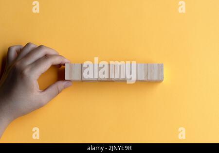 Hand berührt sechs Holzblock auf gelbem Hintergrund Stockfoto