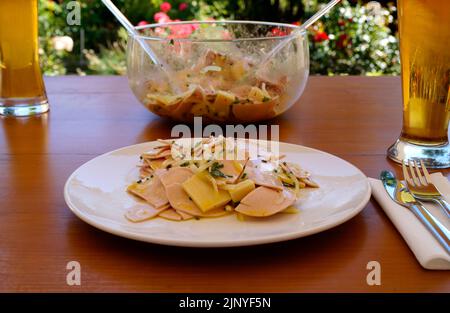 Ein traditionelles, rustikales und herzhaftes deutsches Abendessen in einem Biergarten mit ein paar Bieren, einem Schweizer Wurstsalat mit Käse und Zwiebeln Stockfoto