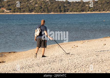 20. Juli 2022: Person, die am leeren Kiesstrand mit einem Metalldetektor im Freien läuft Stockfoto