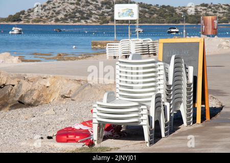 13. Juli 2022: Plastikliegen und Sonnenschirme an einem leeren Strand in Kroatien Stockfoto