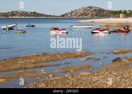 13. Juli 2022: Wasserroller und kleine Boote, die an einer Birne an einem leeren Strand in Kroatien festgemacht sind Stockfoto