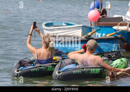 West Mersea Regatta auf Mersea Island in Essex. Ein Mann und eine Frau in aufblasbaren Kajaks, die ihre Mobiltelefone benutzen. Stockfoto