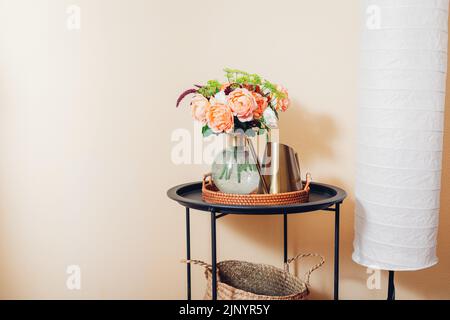 Frisches Bouquet von orangefarbenen englischen Rosen Blumen in Vase auf dem Tisch mit Gießkanne von Stehlampe gelegt. Innenausstattung und Einrichtung des Hauses. Platz Stockfoto
