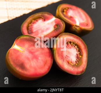 Schwarze Hälften von Tomaten auf schwarzem Steinbrett Stockfoto