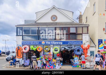 In einem Geschäft von The Cobb in Lyme Regis an der Jurassic Coast in Dorset, Südengland, werden am Straßenrand bunte Schlauchboote und Strandspielzeug ausgestellt Stockfoto