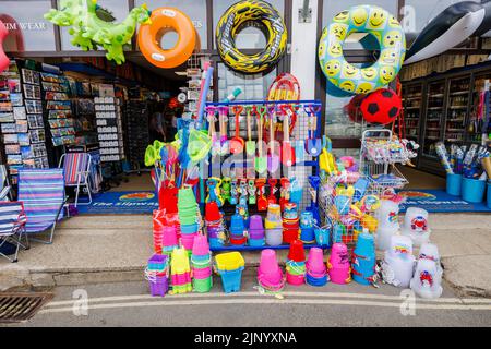 In einem Geschäft von The Cobb in Lyme Regis an der Jurassic Coast in Dorset, Südengland, werden am Straßenrand bunte Schlauchboote und Strandspielzeug ausgestellt Stockfoto