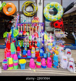 In einem Geschäft von The Cobb in Lyme Regis an der Jurassic Coast in Dorset, Südengland, werden am Straßenrand bunte Schlauchboote und Strandspielzeug ausgestellt Stockfoto