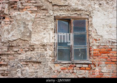 Das Äußere des alten zerfallenden Gebäudes hat ein einzelnes Fenster mit einem Holzrahmen, der 6 kleine Glasscheiben hat. Sehen Sie eine Nahaufnahme einer Ziegelmauer in Kroatien. Stockfoto