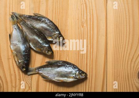 Getrockneter geräucherter Fisch, auf einem leichten Holzbrett, Ansicht von oben. Vier getrocknete Fische auf einem hölzernen Hintergrund. Stockfoto