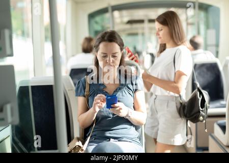 Positive Frau lesen vom Mobiltelefon in der Kabine von Bus oder Straßenbahn Stockfoto