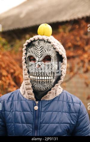 Unschärfe Halloween Menschen Porträt. Person in Sensenmann Maske auf Natur Herbst Hintergrund stehend hält Apfel auf dem Kopf. Halloween-Horror. Schädel ghos Stockfoto