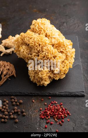 Rohe Sparassis (Blumenkohlpilz), Hericium, Clavaria (Korallenpilz) auf schwarzem Betongrund mit Salz und Gewürzen. Seitenansicht. Stockfoto