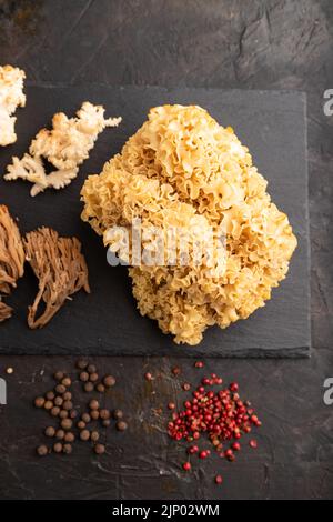 Rohe Sparassis (Blumenkohlpilz), Hericium, Clavaria (Korallenpilz) auf schwarzem Betongrund mit Salz und Gewürzen. Draufsicht, flach liegend. Stockfoto