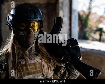 Porträt einer Frau in einem Helm und einer Brille mit einem Maschinengewehr in den Händen. Eine Soldatin in Tarnuniform hält eine Waffe. Stockfoto