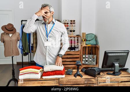 hispanischer Mann mittleren Alters, der als Manager in einer Einzelhandelsboutique arbeitet und mit der Hand in schockbedeckendes Gesicht und Augen blickt und mit Verlegenheit durch die Finger schaut Stockfoto