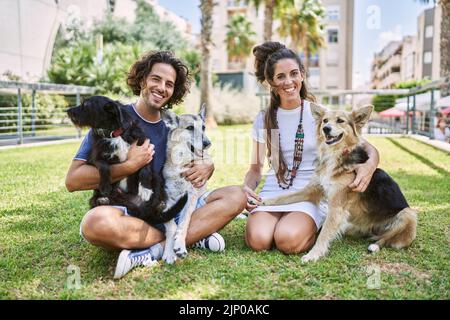 Mann und Frau Paar lächeln selbstbewusst auf Kraut mit Hunden im Park sitzen Stockfoto