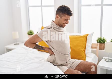 afroamerikanischer Mann, der an Rückenschmerzen leidet und im Schlafzimmer auf dem Bett sitzt Stockfoto