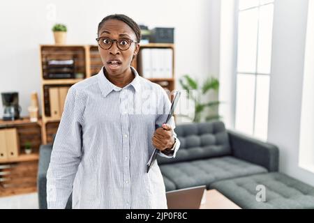 Afrikanische Frau, die in der Psychologieklinik im Schockgesicht arbeitet, skeptisch und sarkastisch aussieht, überrascht mit offenem Mund Stockfoto
