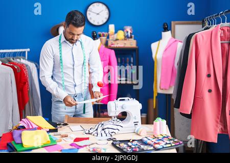 Junger hispanischer Mann, Schneider, der im Nähstudio Dokument liest Stockfoto