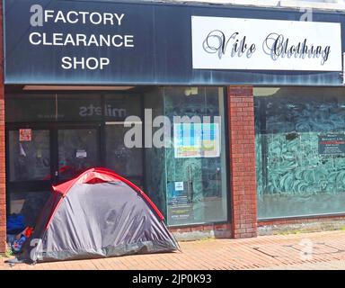 Eine verlassene geschlossene Modehauserei, mit Obdachlosenschlafplatz, mit Zelt im Ladeneingang, Mill Street, Macclesfield, Heshire, England Stockfoto