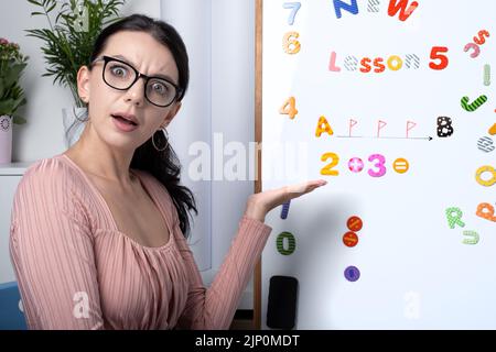 Eine Grundschullehrerin fragt nach der Antwort auf ein einfaches Beispiel in Mathematik. Eine Lehrerin unterrichtet Mathematik online über eine Webcam. Bildung Stockfoto