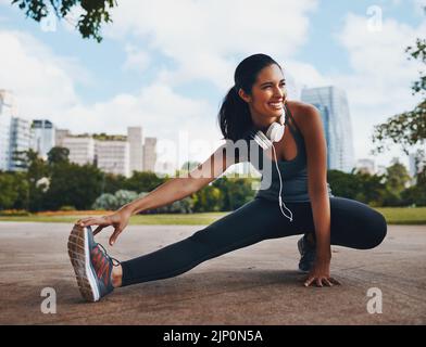 Lächeln Sie sich auf Ihren Weg zur Fitness. Ganzkörperaufnahme einer attraktiven jungen Sportlerin, die im Freien Stretchübungen in der Stadt macht. Stockfoto