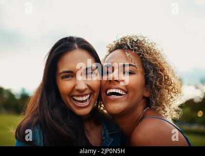 Wir ergänzen uns gegenseitig. Beschnittenes Porträt von zwei attraktiven jungen Freundinnen, die lächeln, während sie in einem Park zusammen stehen. Stockfoto