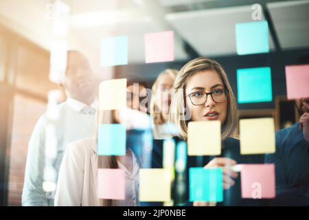 Der Teamleiter plant Ideen und schreibt auf Haftnotizen, während er spricht und zeigt Vision und Innovationsstrategie. Vielfältige Gruppe kreativer Geschäfte Stockfoto