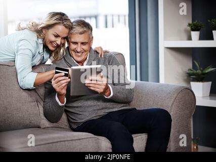 Das sieht aus wie ein absoluter Diebstahl. Ein reifes Paar, das ein digitales Tablet und eine Kreditkarte verwendet, um zu Hause online einkaufen zu können. Stockfoto
