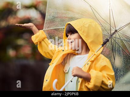 Regnerisches Wetter ist meine Lieblingswetterart. Ein entzückender kleiner Junge im Regen draußen. Stockfoto